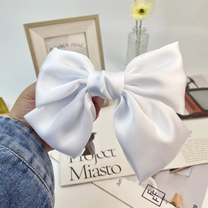 Detail of a large white satin bow hair clip with elegant silk texture and glossy finish