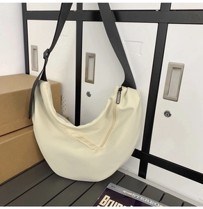 Detail of cream crescent crossbody bag with adjustable wide black strap and sleek zipper