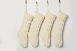 Set of four beige cable-knit Christmas stockings hanging on a minimalist white wall