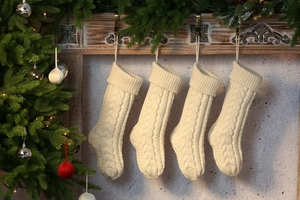 Close-up of four cream knitted Christmas stockings with cable pattern hung on a fireplace