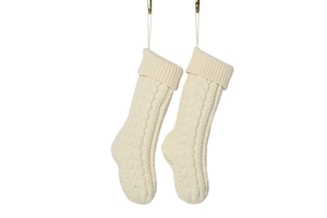 Detail of two off-white cable-knit Christmas stockings with hanging loops on white background