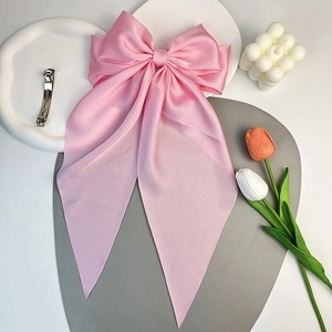 Detail of a large pink satin bow hair clip styled with tulips and a bubble candle