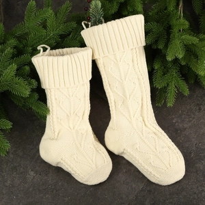 Cream knit Christmas stockings with cable patterns and green pine on dark stone background