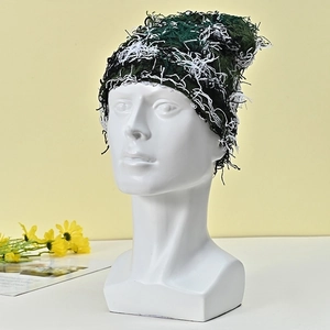 Detailed view of dark green and white knitted beanie featuring fuzzy tassel textures