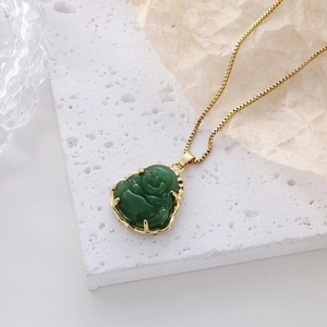 Deep green emerald Buddha pendant necklace with a fine golden chain on a stone plate