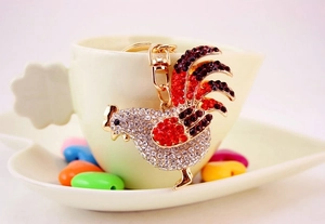 Close-up of golden rooster keychain with sparkling rhinestones on a ceramic cup