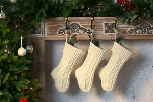 Three cream knitted Christmas stockings with cable patterns hanging on a decorated mantel