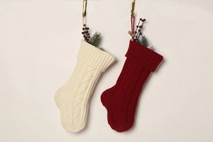 Detail of cable knit Christmas stockings in ivory and dark red with festive berry accents