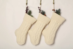 Three cream knit Christmas stockings with pine needles and red berries on gold hooks