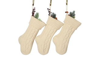 Close-up of knit Christmas stockings with cable patterns, red berries, and pine cones