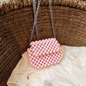 Handmade pink beaded crossbody bag with silver chain strap on a rustic background