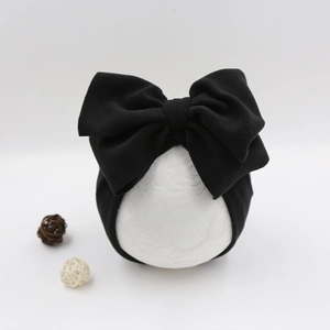 Detail of baby turban featuring a large black bow design on a white model head