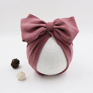 Detail of baby turban hat in dusty rose with large bow on white lace display stand