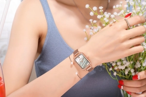 Close-up of a rose gold rectangle quartz watch with green dial on a woman's wrist