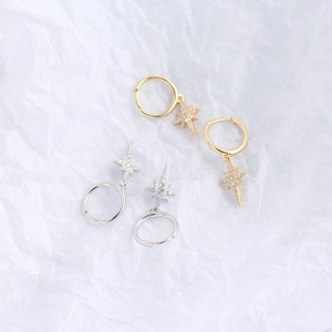 Detailed view of silver and gold eight-pointed star earrings with zircon on textured paper