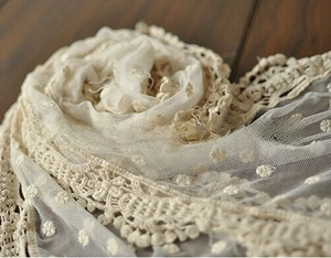 Close-up of cream lace scarf with intricate crochet floral embroidery on dark wood surface
