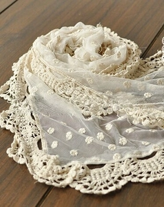 Detail of cream lace scarf showing floral embroidery and crochet lace borders on wood