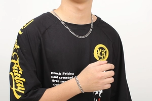Detail of silver Cuban link necklace and bracelet set worn by male model on white background