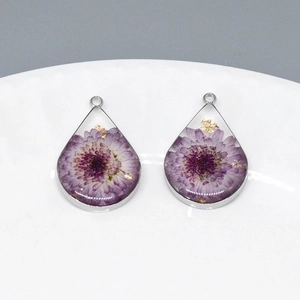 Macro detail of tear drop resin pendants with purple dried flowers and gold flakes