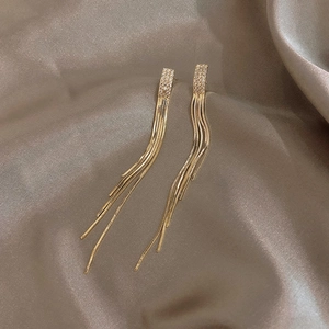 Dettaglio di orecchini a nappa dorati con strass su elegante tessuto in seta champagne