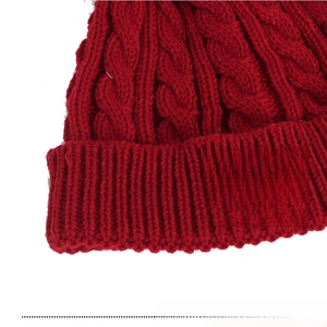 Close-up of red cable knit winter hat showing the soft texture and faux leather logo label