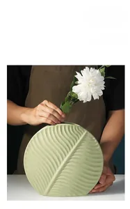 Detailed texture of leaf-shaped light green ceramic vase held by hands, light up your home