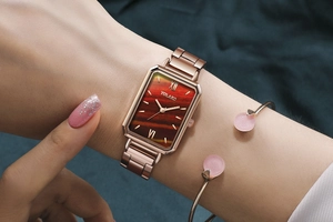 Detail of rose gold square watch with red textured dial and matching jewelry