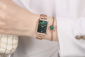 Close-up of rose gold rectangular watch with green dial and matching gemstone bracelet