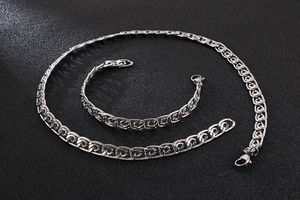 Detailed view of silver embossed stainless steel necklace and bracelet set on black background
