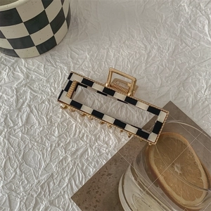 Detailed close-up of large black and white checkerboard hair claw with gold metal frame