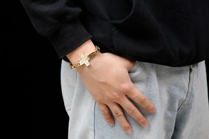 Close-up of men's gold titanium cross bracelet styled on model with black hoodie