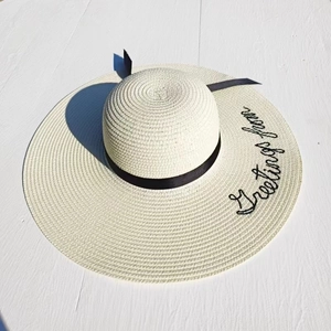 Detail of cream straw sun hat with black ribbon and Greetings from embroidery on brim