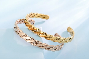 Detail of twisted cable cuff bracelets in gold and rose gold on a geometric stand