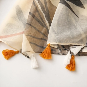 Détail de l'écharpe en lin beige avec motif de feuilles brunes et franges orange
