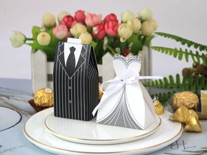 Close-up of tuxedo and wedding dress candy boxes with silk bow on a white plate