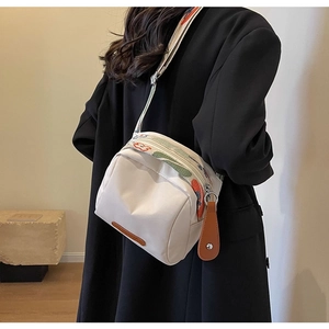 Detail of white shell bag with colorful patterned strap and brown leather zipper pull