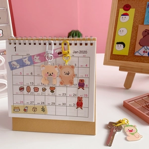 Cute Japanese acrylic bear keychains in white and yellow hanging on a desk calendar