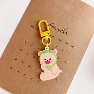 Detail of cute acrylic bear keychain with green hood and yellow metal clasp on paper