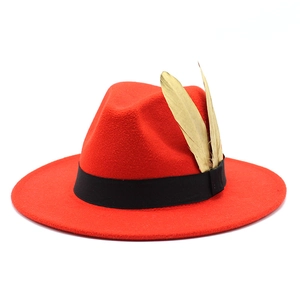 Detail of red wool fedora hat featuring a black ribbon and two striking gold feathers