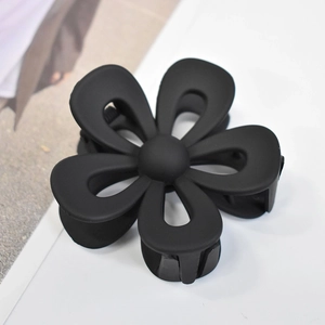 Macro detail of matte black flower hair claw clip with smooth paint finish on white background