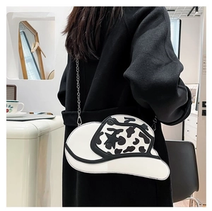 Detail of cowboy hat shaped crossbody bag with black and white cow print and chain strap