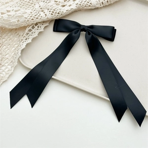 Close-up of black satin double bow hair clip with long ribbons on a white tray
