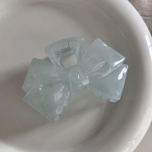 Close-up of a blue bow-shaped shark hair claw clip resting on a white ceramic plate
