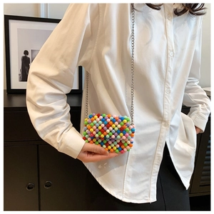 Detail of colorful beaded crossbody bag with silver metal chain on white shirt