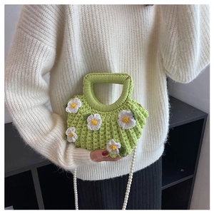 Detail of a green handmade crochet shell bag with white flowers and a pearl strap