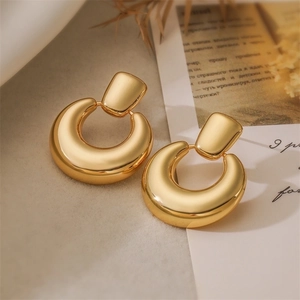 Close-up of golden geometric hoop earrings on a beige fabric background with dried flowers