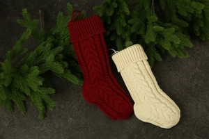 Detail of red and cream cable-knit Christmas stockings on dark stone with pine branches