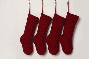 Row of four red cable knit Christmas stockings hanging on hooks against white wall