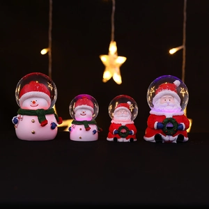 Close-up of four glowing Christmas crystal balls with Santa Claus and snowman figurines