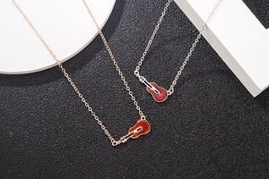 Detail showing two guitar-shaped pendants in rose gold and silver on a minimalist base